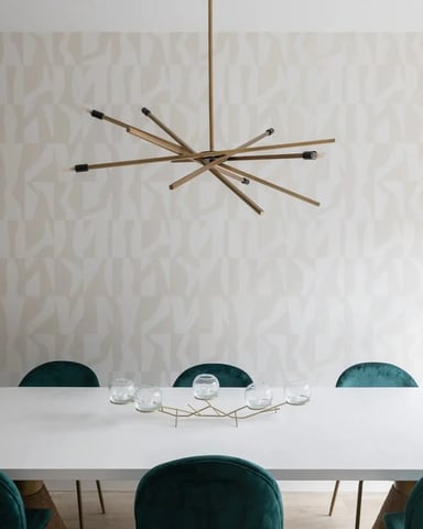 Modern dining room with oval white table, teal velvet chairs, brass starburst pendant light, and patterned wallpaper.