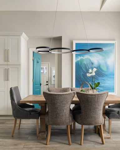 Open-plan kitchen and dining area with wooden table, upholstered chairs, modern pendant light, and ocean wave artwork on wall