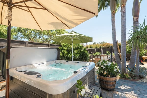 Hot tub with bubbling water under beige umbrella on patio with palm trees and green umbrella in background